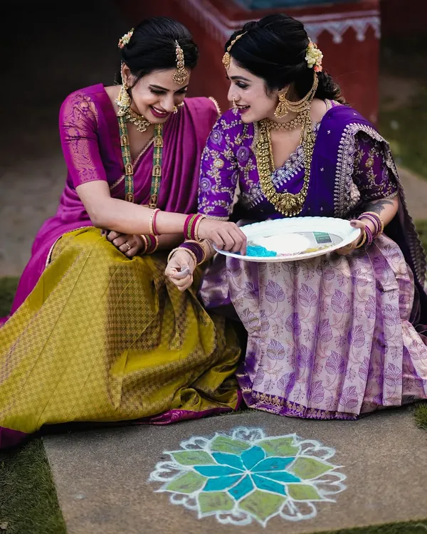A beautiful, candid moment between two women during a Sankranti festival shoot, sharing a smile over a traditional rangoli.