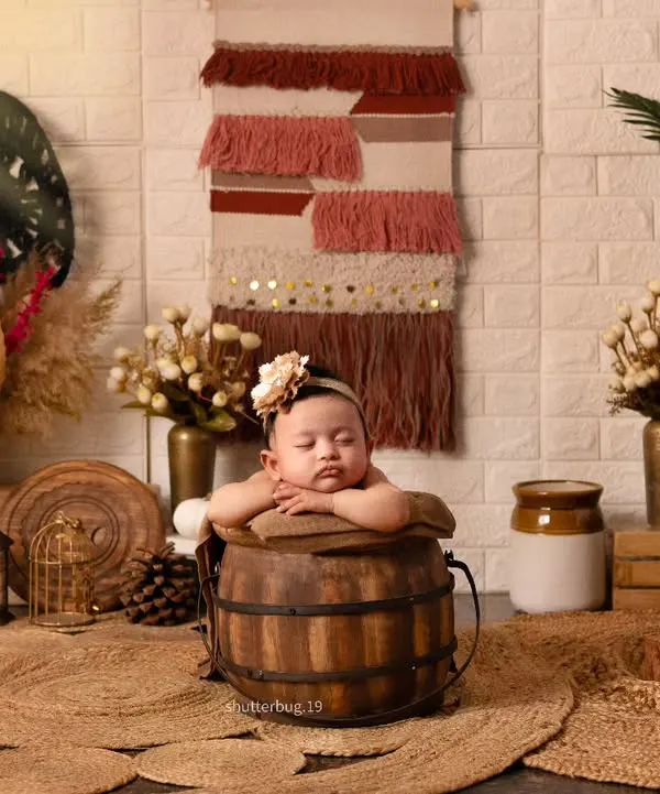 A perfect pose. This baby is resting their arms on the edge of a rustic wooden bucket, creating an incredibly sweet and relaxed portrait within our earthy boho setup.