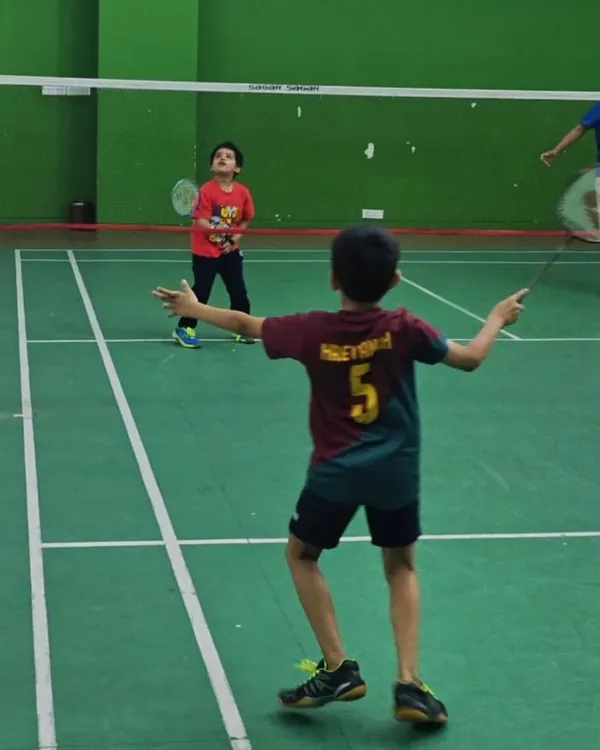 A young player gets ready to return a shot during a doubles game. Introducing match play early helps kids understand court positioning and strategy in a real-game scenario.