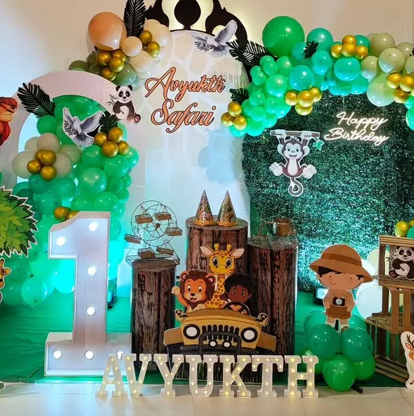 A complete jungle safari setup for a first birthday, featuring a grass wall, marquee number '1', animal cutouts, and a green and gold balloon arch.