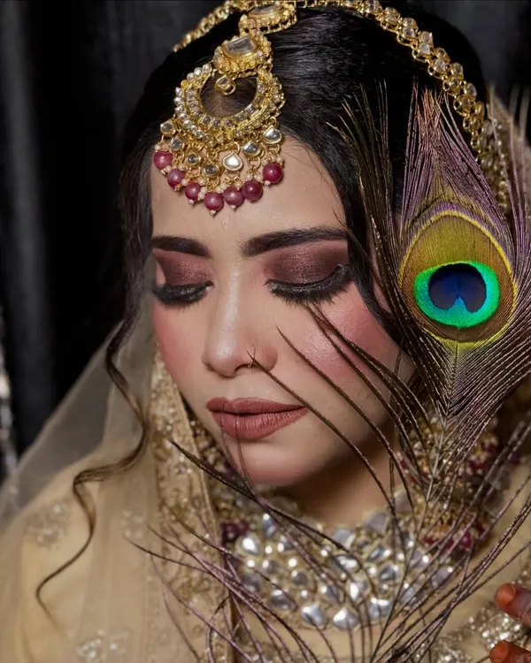 A creative shot featuring a peacock feather. The deep, smoky eye makeup and nude lip create a dramatic and artistic look, perfect for a themed photoshoot.