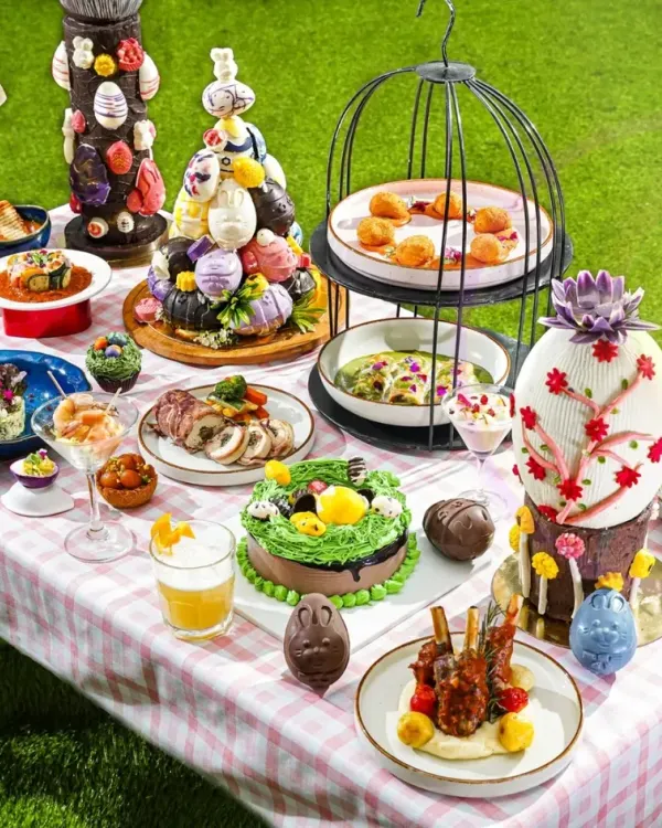 A whimsical Easter brunch fantasy. We created a full tablescape with a pastel checkered cloth, lush green grass, and an abundance of themed treats like bunny cakes and chocolate eggs. This wide shot captures the magical, celebratory atmosphere of the entire spread.