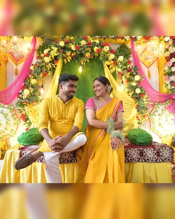 A beautiful couple framed by our classic Haldi ceremony decor. The setup combines a dense floral arch, bright yellow and pink draping, and traditional umbrellas for a complete and festive look.