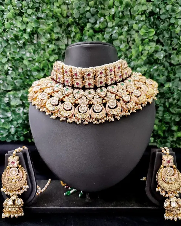 A quintessential bridal choker set in kundan style, featuring half-moon motifs and accented with red and green stones. This is a timeless piece available for rent.