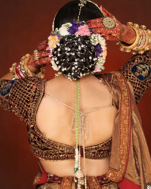This intricate bridal bun is a testament to advanced hairstyling techniques. The style features a woven pattern, adorned with fresh flowers and delicate pearl chains for a classic and elegant bridal look.