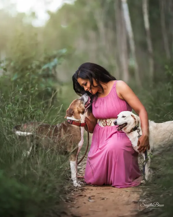 The pure, uncomplicated love between a woman and her dogs. This outdoor portrait captures a tender moment of connection in a beautiful, natural setting. The soft light filtering through the trees adds a magical quality to this heartwarming scene.