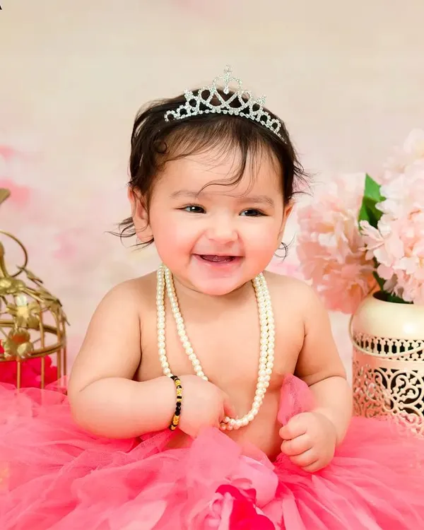 A joyful portrait of a baby girl celebrating her first birthday, dressed in a pink tutu and a sparkling tiara, her smile lighting up the room. This is the kind of magical moment I love to create for your family to treasure.