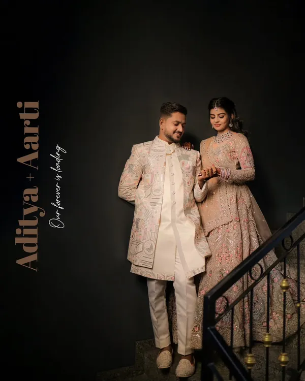 An elegant portrait of a couple in beautifully coordinated ethnic wear, posed on a staircase. The dark background makes their luxurious outfits and connection stand out.