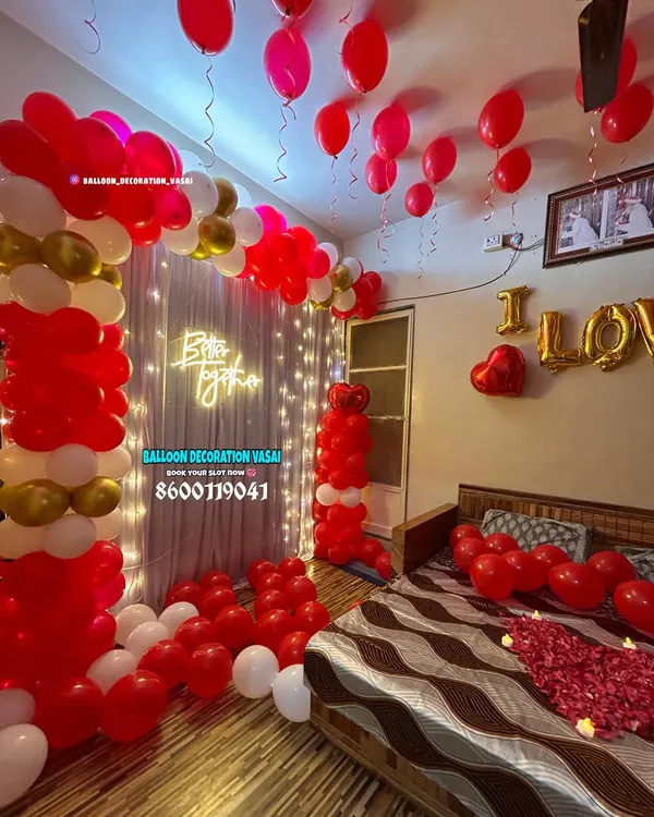 This is a complete romantic room takeover, featuring red and gold balloon columns, a "Better together" neon sign, and a bed decorated with rose petals and "I LOVE YOU" foil balloons.