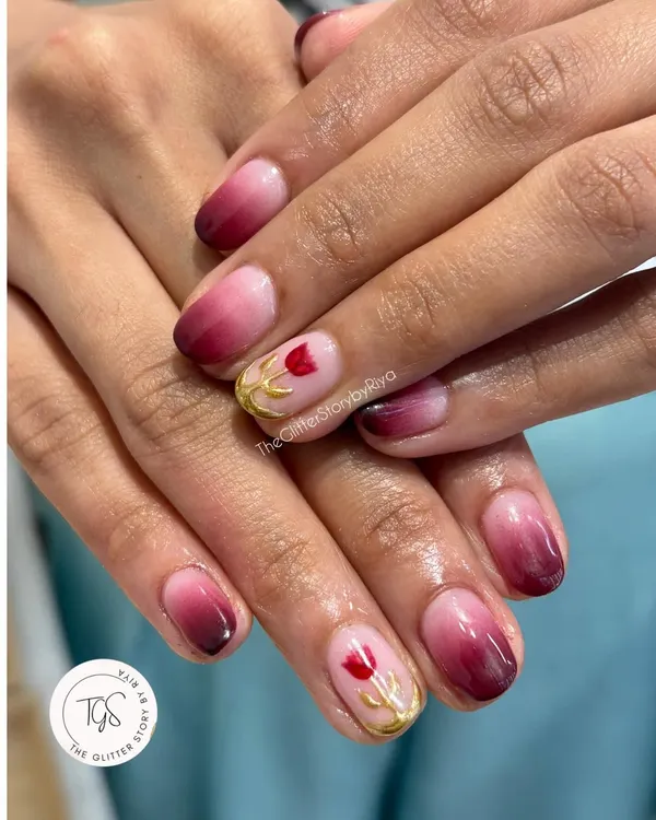 A beautiful ombré set with a touch of hand-painted artistry. The nails feature a deep red to pink fade, with a delicate tulip painted in gold on the accent nail.