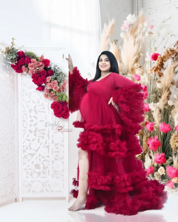 A stunning portrait of an expectant mother in a voluminous, ruffled red tulle gown. This shot, taken against a backdrop of beautiful florals, showcases the glamour and elegance I bring to my studio maternity sessions.
