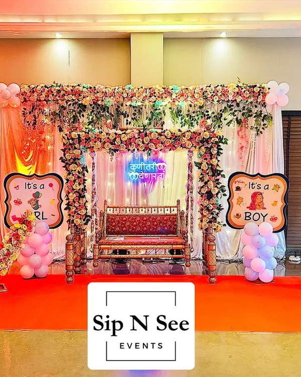 A complete stage setup for a baby shower at Lodha Amara's clubhouse. This decoration includes a floral jhula, a 'Kunitari yenar ga' neon sign, gender reveal props, and a floral moon seat, covering all the essentials for a grand celebration.