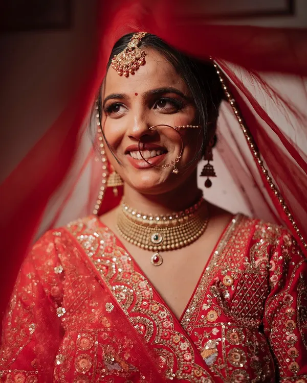 A radiant close-up of a bride, her joyful smile captured from under her red veil. This shot beautifully highlights her happiness and traditional bridal jewelry.