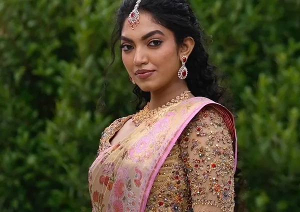 A portrait of a bride in her custom ensemble. The heavily embellished zardozi blouse perfectly complements the soft pink and gold tones of her floral silk saree, creating a look of pure elegance.