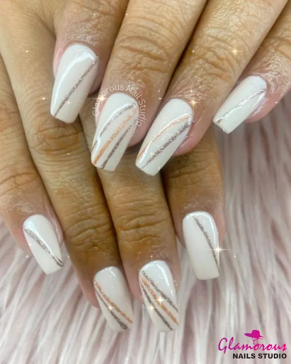 A perfect example of sophisticated elegance. This design features a creamy white base on long, coffin-shaped nails, adorned with delicate, sparkling stripes in silver and rose gold.