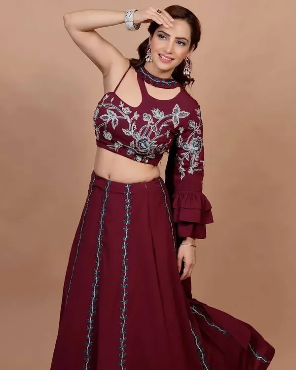 This maroon Indo-Western lehenga is all about modern style. The outfit features a unique one-shoulder blouse with a cutout detail and bell sleeve, paired with a flowing skirt. The blouse is adorned with beautiful floral embroidery.