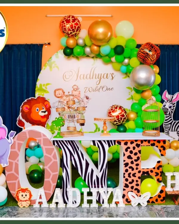 A full-stage jungle theme for a "Wild One" first birthday. This setup features character cutouts of a lion, elephant, zebra, and giraffe, large 'ONE' marquee letters with animal prints, and a lush green and gold balloon arch.