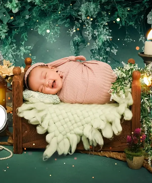 A baby smiles in their sleep while nestled in a tiny bed in an enchanted forest setup. The warm candlelight and magical sparkles create a truly dreamy atmosphere for this newborn portrait.