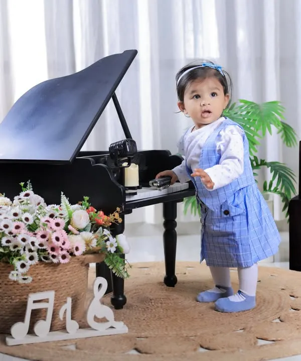 Celebrating her first birthday with a musical theme. This little girl looks adorable standing by our miniature grand piano, a perfect prop for a classic and elegant milestone photoshoot.