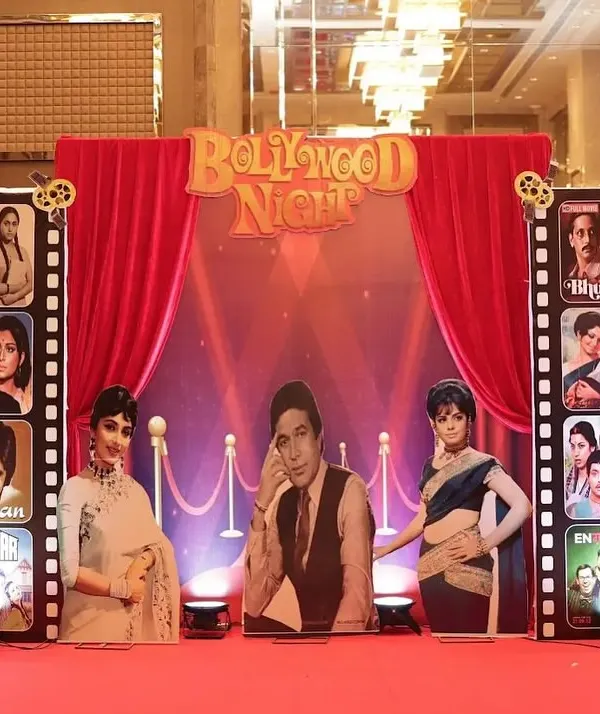 The main stage for a 60th birthday, designed with a 'Bollywood Night' retro theme. We used a red curtain backdrop, film reel props, and cutouts of classic movie stars.