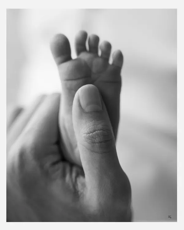 A father's thumb gently holds his baby's entire foot. This timeless black and white image is a powerful illustration of how tiny they are in these first few days.