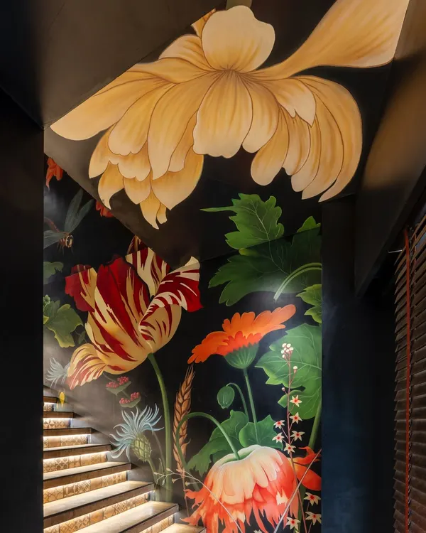 This staircase became a journey through a blooming garden. I wanted the experience of dining here to begin with this climb, where oversized, hand-painted florals on a dark background create a dramatic and immersive prelude to the meal ahead.