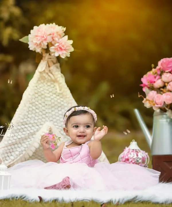 A whimsical outdoor portrait session with a boho-chic theme. This little girl is all smiles in a beautiful pink dress, surrounded by a lace teepee and floral props that create a magical, fairytale-like setting.