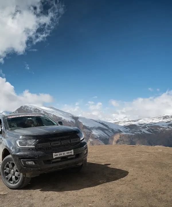 A rugged, all-black Ford Endeavour is parked on a dirt lookout, with the vast, snow-covered peaks of the Himalayas stretching out behind it. This shot emphasizes the vehicle's powerful presence in an extreme environment.