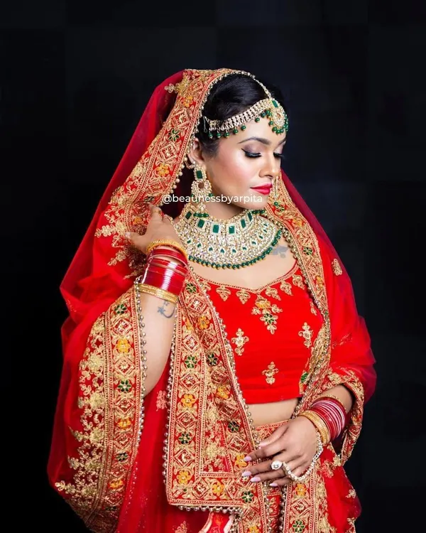 A classic red bridal lehenga with heavy gold embroidery and emerald green jewellery accents. This is a timeless look for the main wedding ceremony, ensuring you look nothing less than a queen.