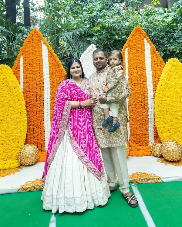 A beautiful family portrait from a Myra ceremony, set against a stunning backdrop of orange and white marigold panels. It's a perfect blend of tradition, celebration, and family love.