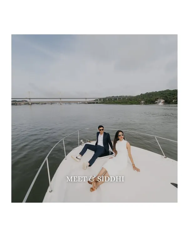 A wide-angle shot of the couple relaxing on the bow of a yacht in Goa. This image captures the feeling of freedom and luxury, with the expansive water and bridge in the background.