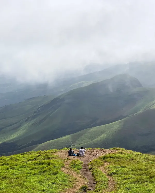Two trekkers finding a moment of peace, gazing out at the endless green valleys of Kudremukha. These are the views that make the climb worth every step.