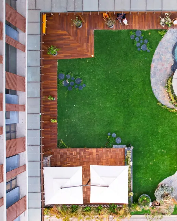 An aerial view of a residential terrace project, showcasing a thoughtful layout that combines lush artificial turf, wooden decking, and a curved stone pathway leading to a jacuzzi and gazebo area.