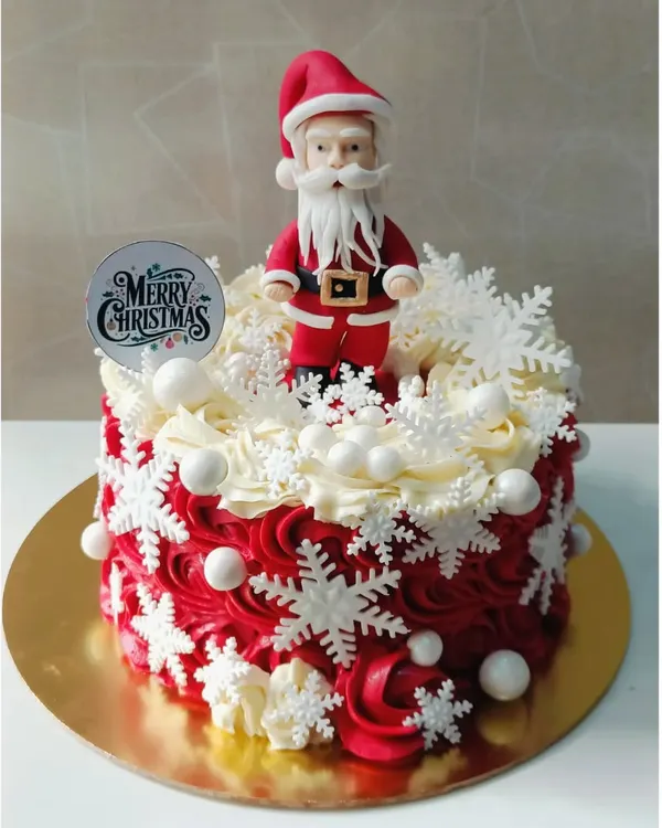 A truly festive Christmas cake, decorated with red and white buttercream swirls, delicate snowflakes, and a handmade Santa Claus topper. This makes a wonderful centerpiece for any holiday table.