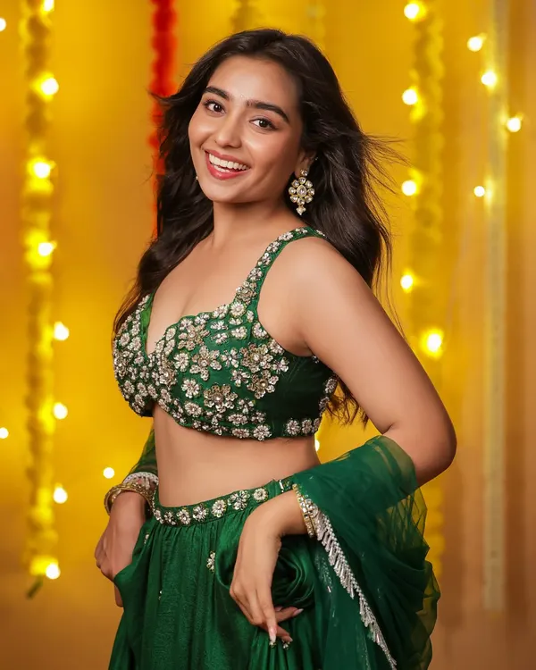 A joyful portrait of a model in a green embroidered lehenga, smiling brightly against a festive background of yellow lights. This shot captures the happy spirit of Diwali.