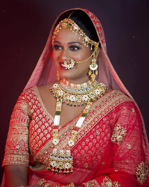 A radiant bride adorned in a magnificent, heavy bridal set featuring Kundan work and green stones. This entire set, from the matha patti to the long necklace, is available for rent.