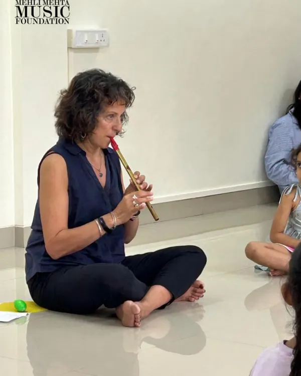 Naheed Shimala uses a simple wind instrument during a class. This demonstrates the use of varied instruments to introduce concepts of pitch, timbre, and breath control in an accessible way for young children.