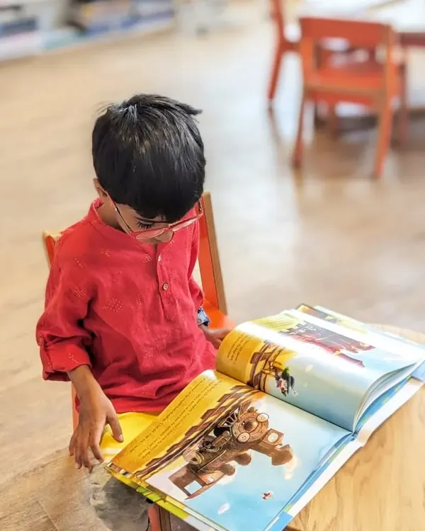 A young bookworm completely absorbed in a picture book. It's moments like these, of quiet focus and discovery, that we aim to create in our cozy reading spaces.