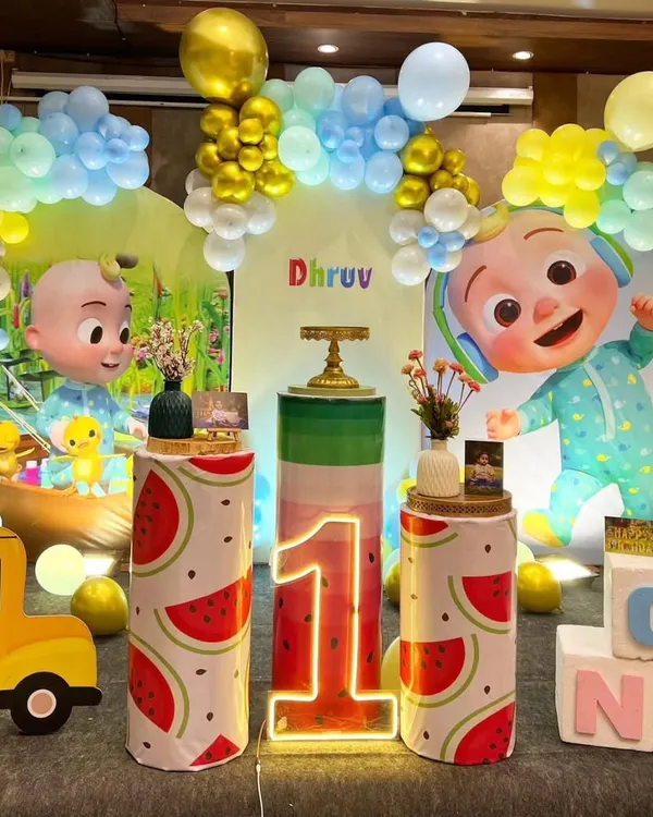 A grand Cocomelon themed first birthday for Dhruv. This elaborate setup includes multiple character cutouts, a Cocomelon bus, watermelon-themed pedestals, and a large, colorful balloon backdrop for an immersive experience.