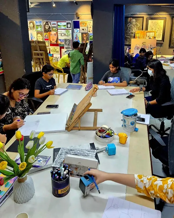 A wide view of a busy workshop session at our studio. Students are gathered around a large table, completely absorbed in their individual art projects.
