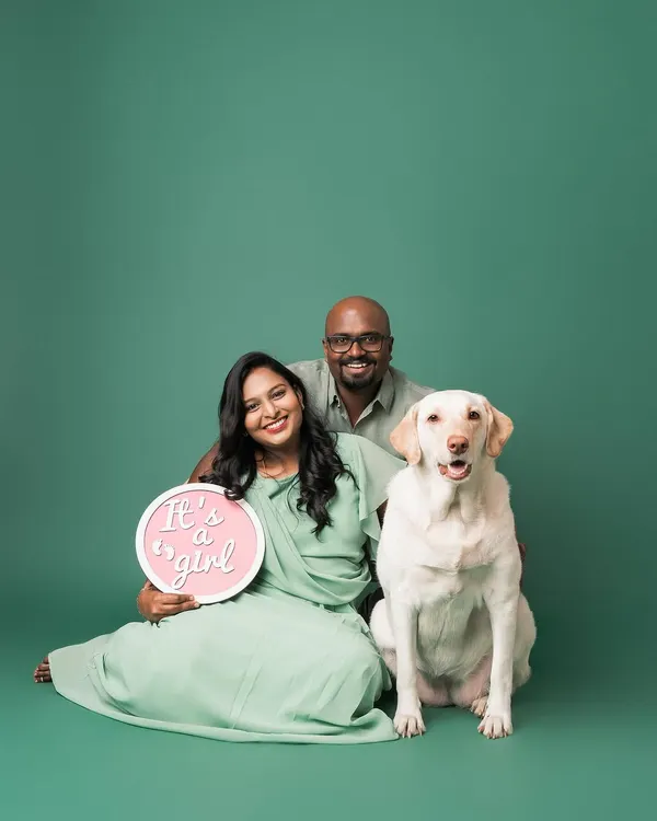 The perfect family announcement! This beautiful couple is joined by their proud Labrador, who is clearly excited to become a big sister. The "It's a girl!" sign adds a lovely touch to this studio maternity portrait.
