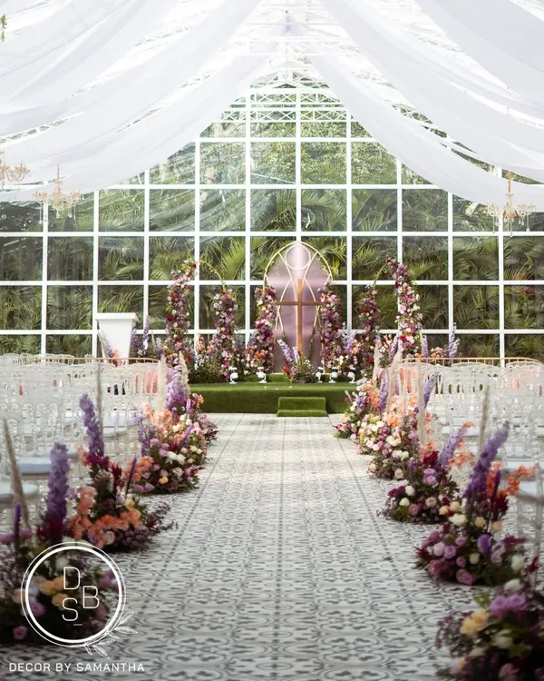 The aisle view of this stunning church-inspired wedding ceremony. The floral-lined path leads to a beautiful altar, all set against a glasshouse backdrop that brings the outdoors in.