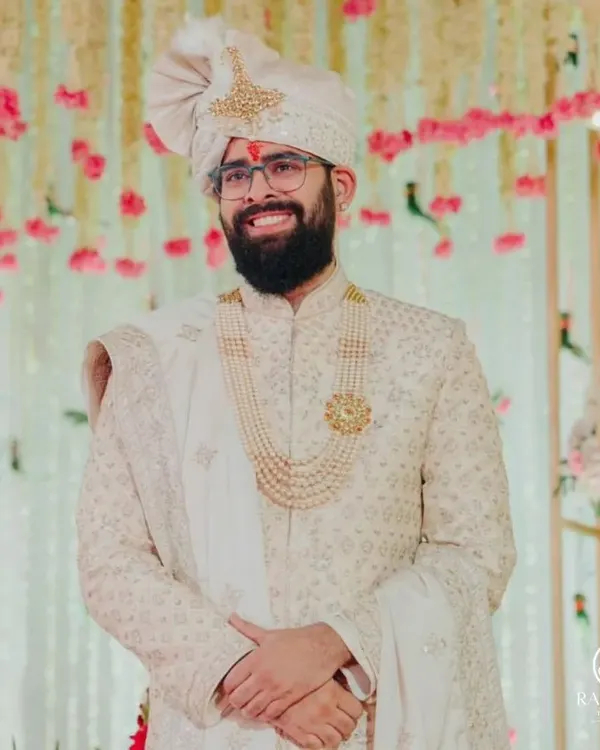 A happy groom on his wedding day, dressed in a classic ivory Shauhar sherwani. His smile says it all, a perfect picture of royal elegance and joy.