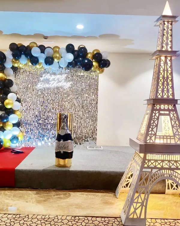A chic Paris-themed birthday setup. This decoration combines a silver sequin backdrop and a black-and-gold balloon arch with our signature light-up Eiffel Tower prop for a touch of international glamour.