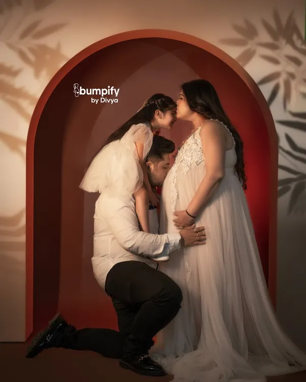 A beautiful family portrait where a father and daughter share a loving kiss with the mom-to-be, all framed within our warm, modern studio arch. This is what it's all about, capturing the love that's about to grow.