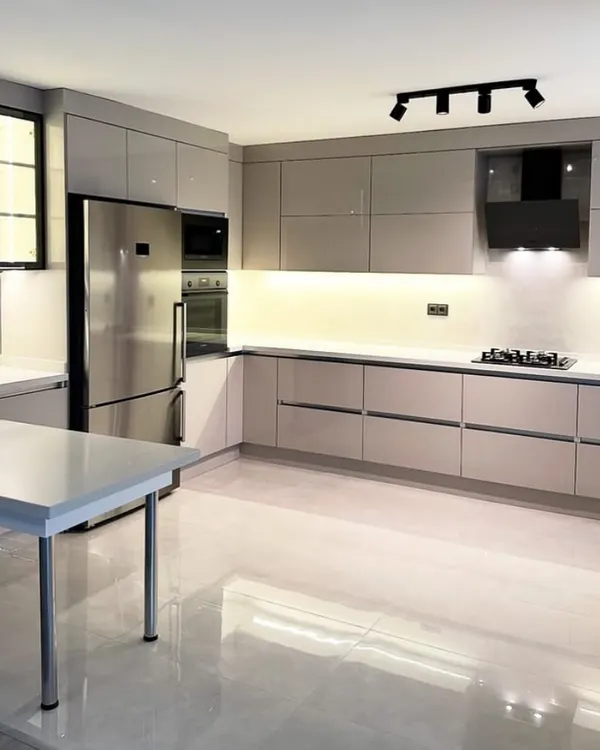 This expansive L-shaped modular kitchen in Gurgaon showcases a sleek, handle-less design with high-gloss grey acrylic shutters. The design features a large, functional island that doubles as a breakfast counter, integrated seamlessly with premium Blum and Hafele hardware for a sophisticated and modern kitchen experience.