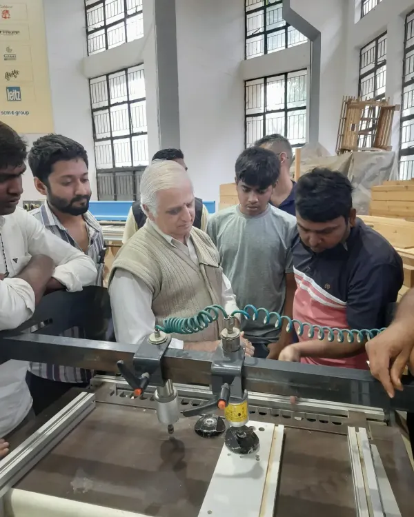 An instructor demonstrates the use of a multi-boring machine to a group of attentive students, a key piece of equipment for creating accurate holes for dowels and hardware.