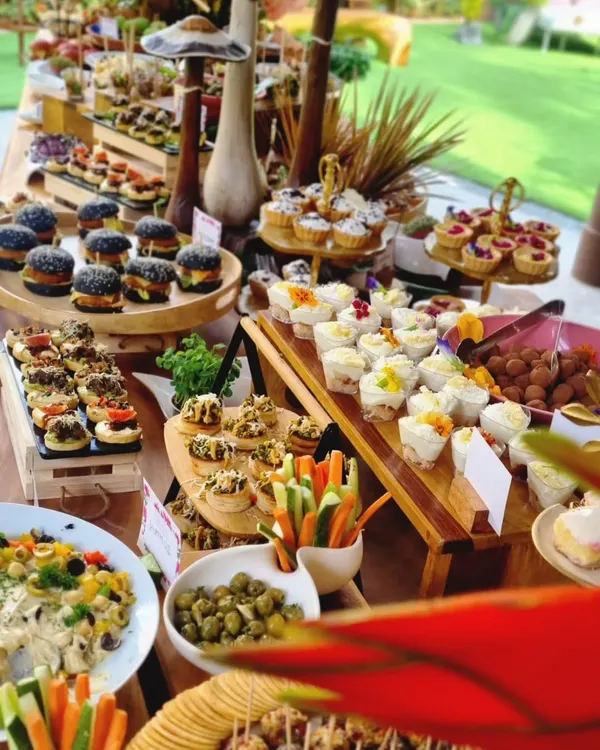 A vibrant and abundant grazing table, showcasing a mix of mini charcoal burgers, assorted canapés, fresh vegetables, and dessert cups. This spread is a perfect example of how we combine diverse flavors and textures for a complete culinary journey.