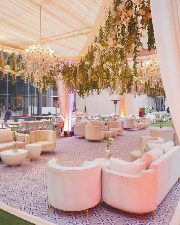 An elegant outdoor lounge setup for a wedding reception, featuring white and cream furniture with beautiful hanging floral arrangements.