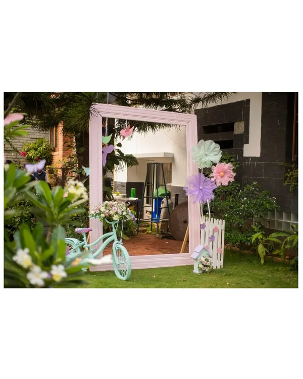 A charming outdoor photo booth we created for a garden party. It features a large pink mirror frame, a mint green bicycle, and whimsical paper flowers.
